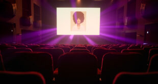 Empty velvet theater seats facing illuminated screen displaying album artwork in elegant London theater at night