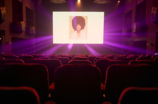 Empty velvet theater seats facing illuminated screen displaying album artwork in elegant London theater at night