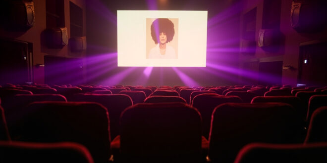 Empty velvet theater seats facing illuminated screen displaying album artwork in elegant London theater at night