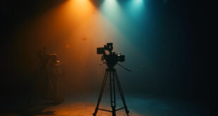 Empty television studio with dimmed lights and dormant camera equipment on tripod, bathed in warm amber and deep blue tones