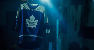 Toronto Maple Leafs jersey hanging alone in empty hockey arena locker room, dramatically lit in blue and white team colors