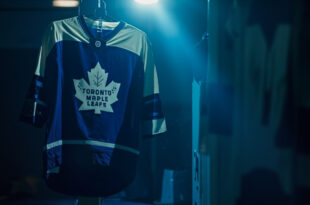Toronto Maple Leafs jersey hanging alone in empty hockey arena locker room, dramatically lit in blue and white team colors