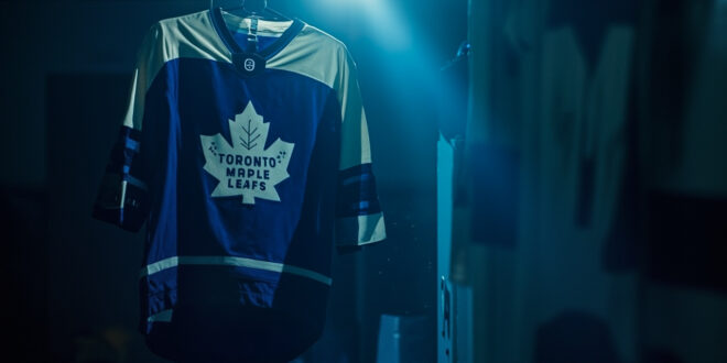 Toronto Maple Leafs jersey hanging alone in empty hockey arena locker room, dramatically lit in blue and white team colors