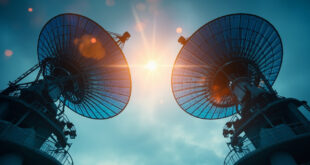 Twin broadcasting towers with satellite dishes silhouetted against dawn sky at modern media complex