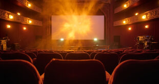 Empty vintage cinema with velvet seats facing a blank screen, film reels and projection equipment illuminated in amber light