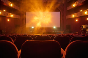 Empty vintage cinema with velvet seats facing a blank screen, film reels and projection equipment illuminated in amber light