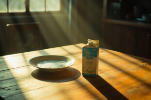 Medical nutrition juice box sits alone on ceramic plate next to empty dinner plate on kitchen table in soft natural light