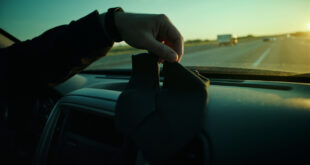 Elegantly tied black necktie rests on empty car seat, with another untied tie on dashboard along quiet empty highway.