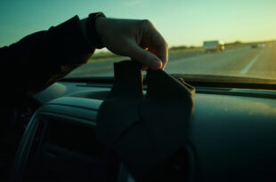 Elegantly tied black necktie rests on empty car seat, with another untied tie on dashboard along quiet empty highway.