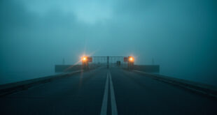 Abandoned coastal border checkpoint at dawn with closed security gate and warning signs overlooking misty waters