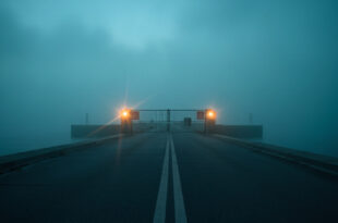 Abandoned coastal border checkpoint at dawn with closed security gate and warning signs overlooking misty waters