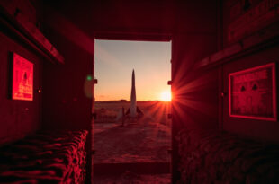 Abandoned ballistic missile standing solitary in dimly lit launch silo at dusk, bathed in red warning lights and gray shadows.