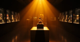 Illuminated Grammy award trophy and music memorabilia displayed in spotlit glass cases within an empty museum gallery