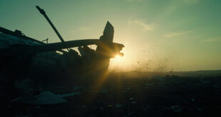Aircraft wreckage scattered across an empty field at dusk, with a broken wing silhouetted against the darkening sky