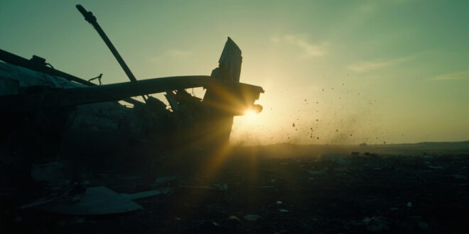 Aircraft wreckage scattered across an empty field at dusk, with a broken wing silhouetted against the darkening sky