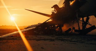 Empty commercial aircraft wreckage with damaged wing debris on abandoned airport tarmac at dusk, illuminated by flames