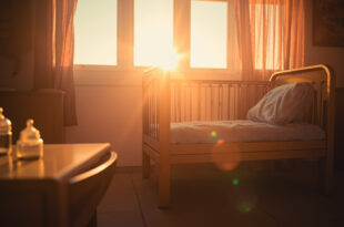 Empty hospital nursery at dawn with an unoccupied crib, folded blankets, and unopened baby bottles awaiting a new arrival