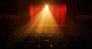 Empty theater seats facing a solitary spotlight illuminating an abandoned Broadway stage, bathed in deep red and gold light