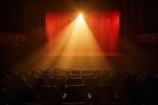 Empty theater seats facing a solitary spotlight illuminating an abandoned Broadway stage, bathed in deep red and gold light