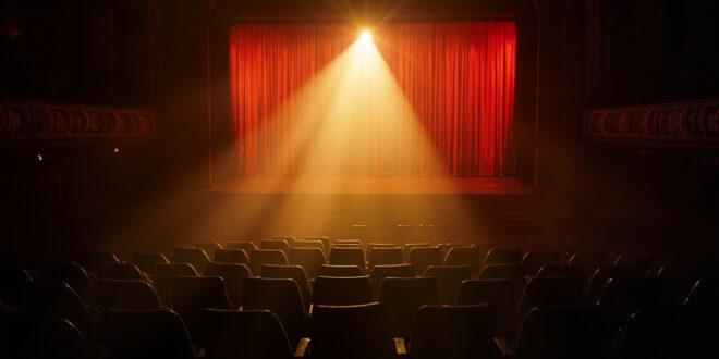 Empty theater seats facing a solitary spotlight illuminating an abandoned Broadway stage, bathed in deep red and gold light