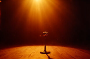 Abandoned vintage microphone under golden spotlight on wooden stage in dimly lit, empty theater hall.