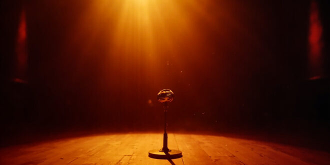 Abandoned vintage microphone under golden spotlight on wooden stage in dimly lit, empty theater hall.