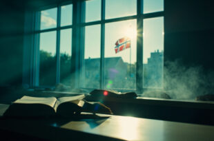 Empty Danish university lecture hall with open books on professor's desk and Danish flag, bathed in Nordic blue light.