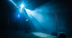Empty microphone stand illuminated by spotlight on abandoned concert stage with unmanned camera equipment after show