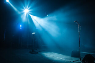 Empty microphone stand illuminated by spotlight on abandoned concert stage with unmanned camera equipment after show
