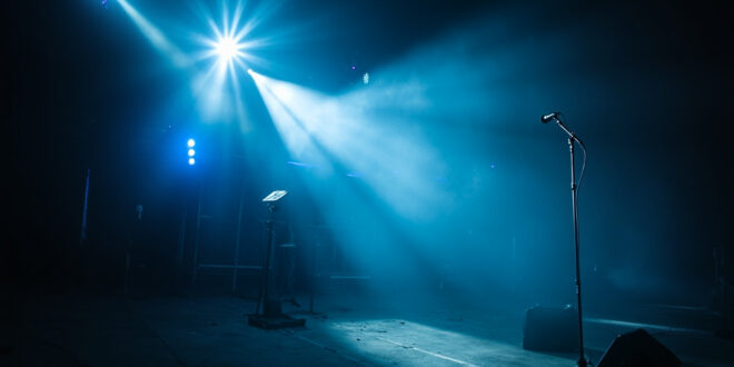 Empty microphone stand illuminated by spotlight on abandoned concert stage with unmanned camera equipment after show