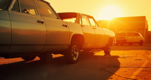 Abandoned car with closed windows reflecting intense sunlight in an empty industrial parking lot under scorching sun
