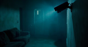 Surveillance camera mounted on wall of empty living room, captured in cold blue lighting suggesting domestic monitoring