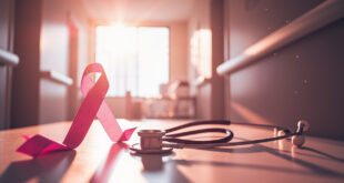 Medical stethoscope and pink awareness ribbon on consultation table in quiet, naturally lit hospital corridor