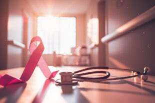 Medical stethoscope and pink awareness ribbon on consultation table in quiet, naturally lit hospital corridor