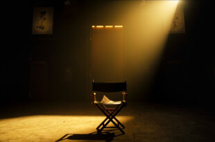 Empty director's chair with script sits under spotlight on dark stage in abandoned movie theater at twilight