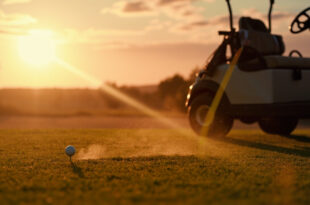 Abandoned golf equipment at golden hour, with clubs leaning against cart and ball on tee on empty emerald green course