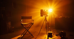Empty director's chair and vintage movie camera in abandoned film studio at twilight, with film reel and script on table