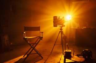Empty director's chair and vintage movie camera in abandoned film studio at twilight, with film reel and script on table