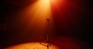 A spotlit vintage microphone stands alone in an empty recording studio, bathed in burgundy and gold light, symbolizing loss.