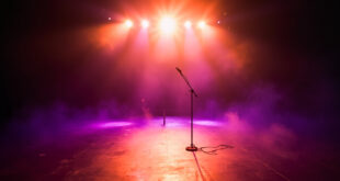 Abandoned concert stage with empty microphone stand illuminated by purple and gold spotlights in vacant venue after show
