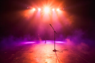 Abandoned concert stage with empty microphone stand illuminated by purple and gold spotlights in vacant venue after show