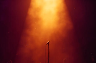 Abandoned microphone stand under golden spotlight on empty concert stage, bathed in deep purple lighting after show
