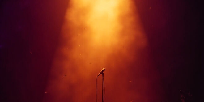 Abandoned microphone stand under golden spotlight on empty concert stage, bathed in deep purple lighting after show