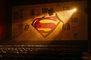 Torn Superman movie poster in dimly lit, deserted theater with empty screen displaying mixed critical reviews.