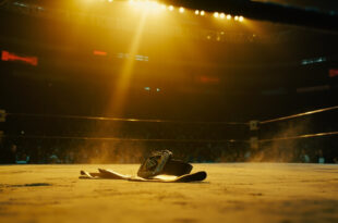 Empty championship belt rests on canvas in a dimly lit, abandoned wrestling ring illuminated by a single spotlight