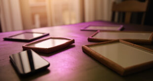 Empty photo frames and smartphone on wooden table in softly lit home interior with warm beige and purple tones
