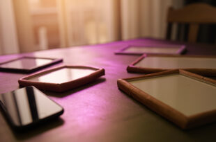 Empty photo frames and smartphone on wooden table in softly lit home interior with warm beige and purple tones