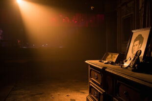 Abandoned theater dressing room with vintage Hollywood photographs on dresser, illuminated by warm amber spotlight in deep shadows