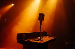 Silent microphone on an empty wooden pulpit stands abandoned in a once-bustling television studio bathed in amber light.
