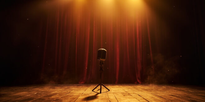 Abandoned vintage microphone stands alone on empty wooden stage in dimmed theater with closed burgundy curtains